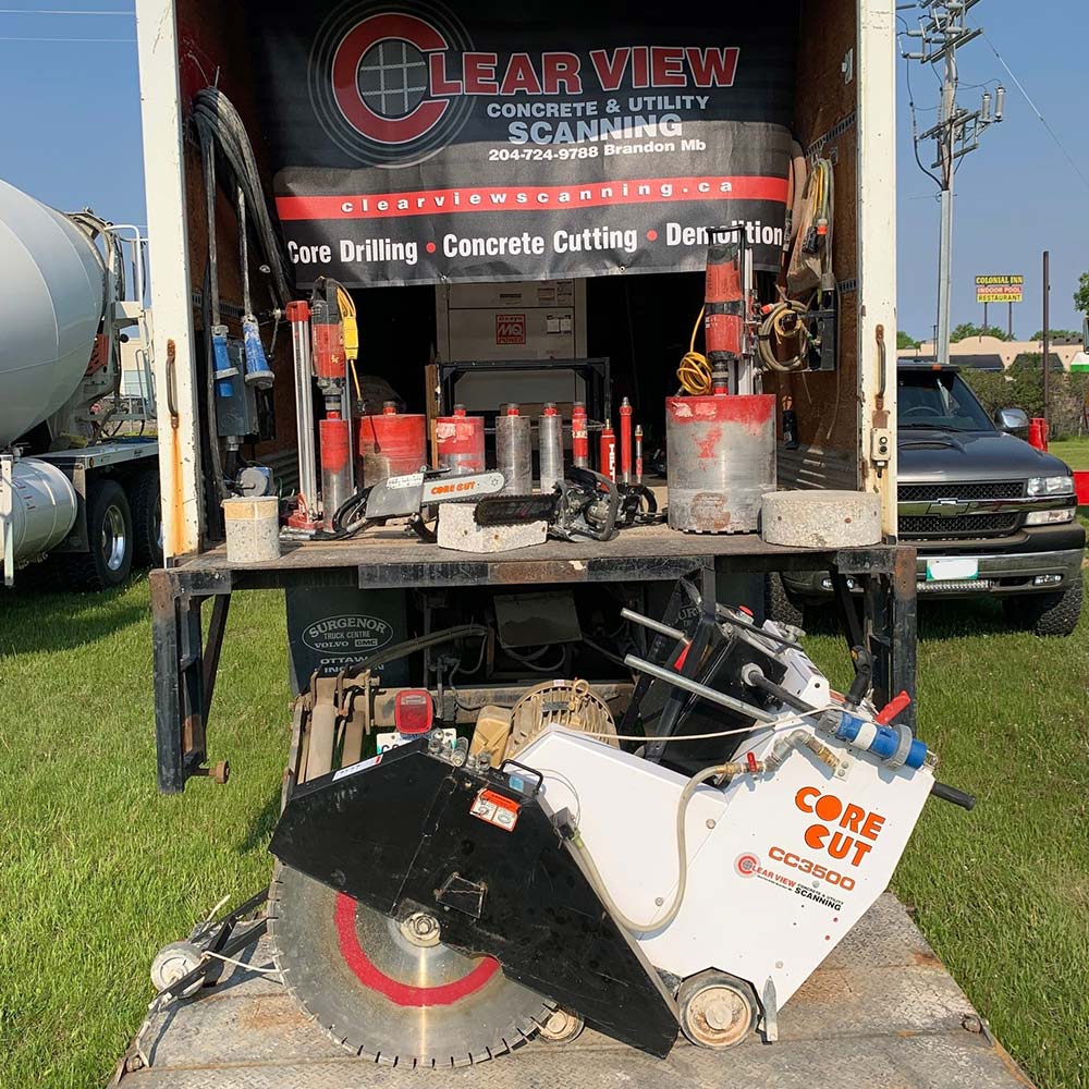 The back of a transport truck loaded with concrete cutting, coring, and drilling equipment. Sitting on the ground in front of the truck is a walk-behind concrete saw.